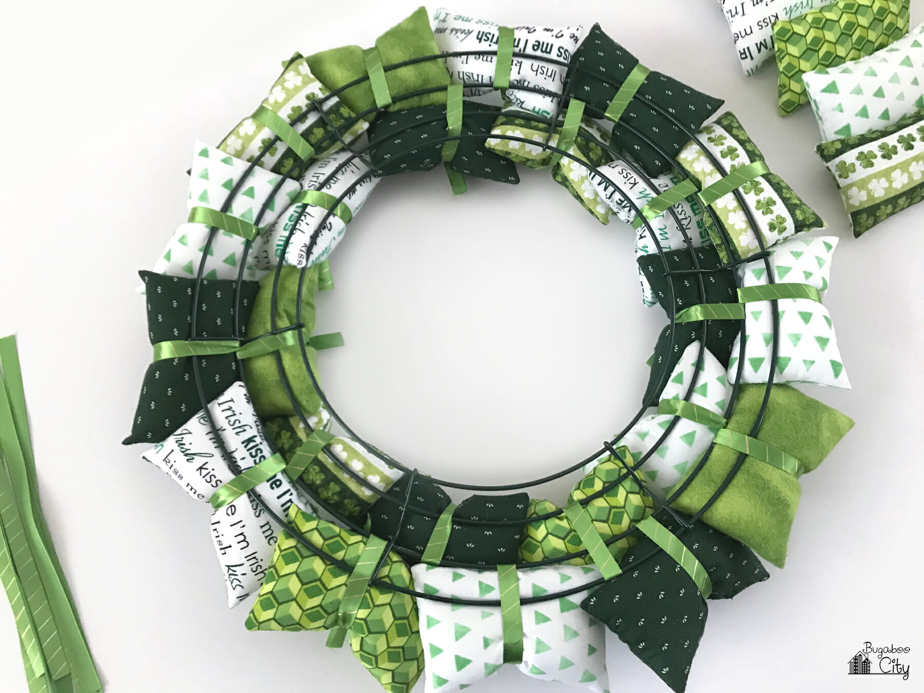 The back of a wire wreath showing fabric pillows attached to it with green ribbon.