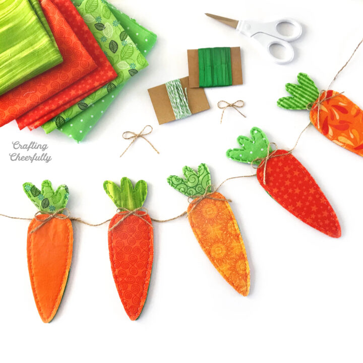 Carrot banner made from fabric scraps on a white table with fabric and ribbon.