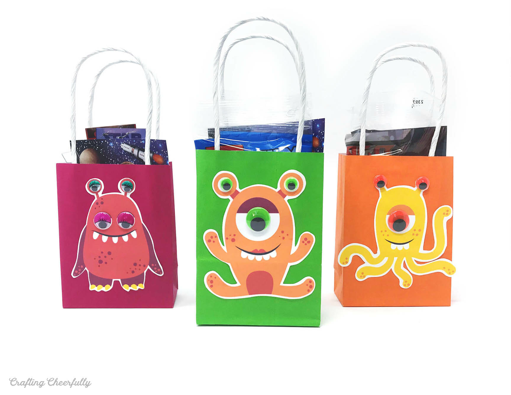 Three small gift favor bags decorated with paper aliens and googly eyes.