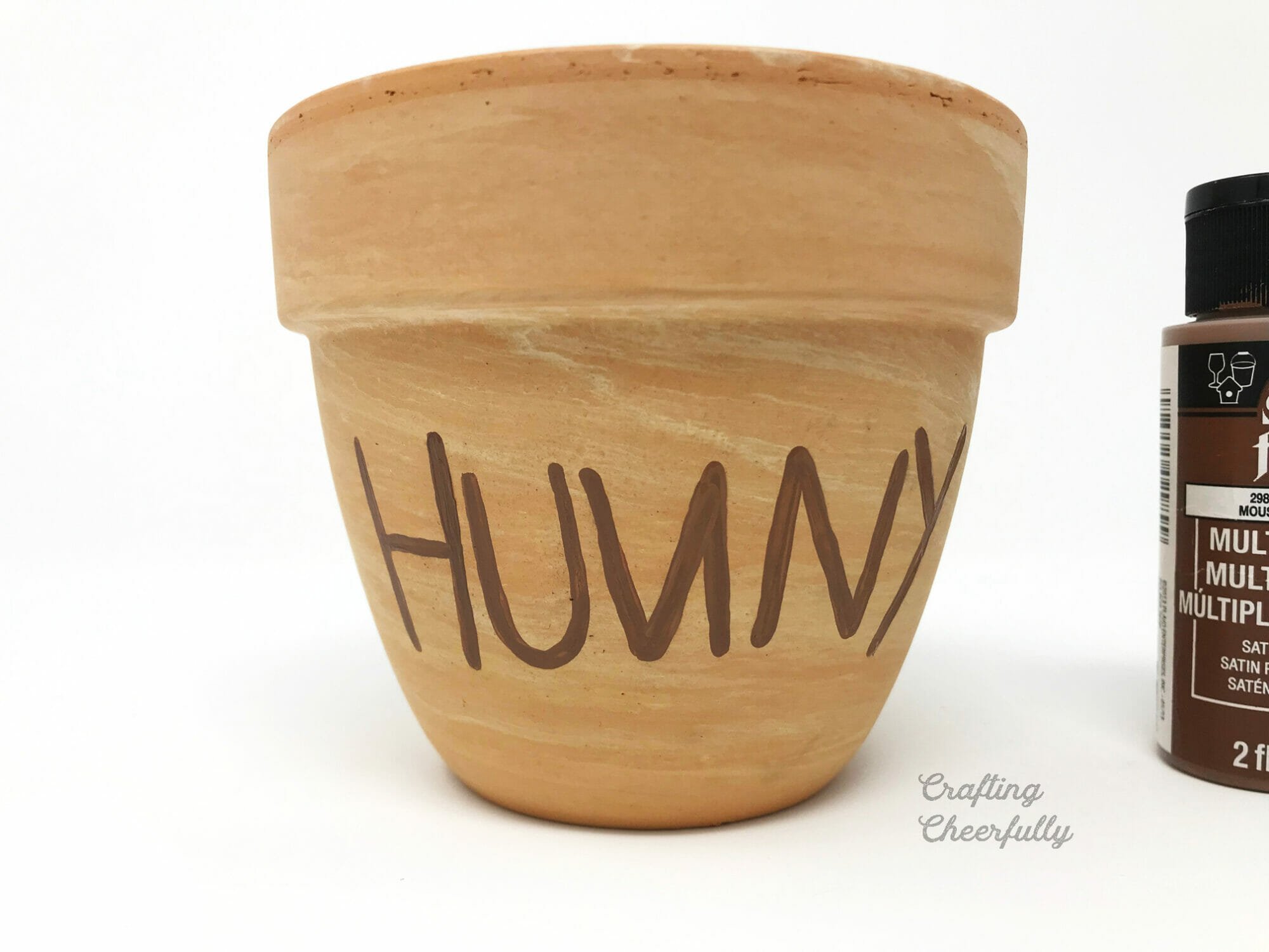 A terra cotta pot with the word HUNNY painted on the front with brown acrylic paint.
