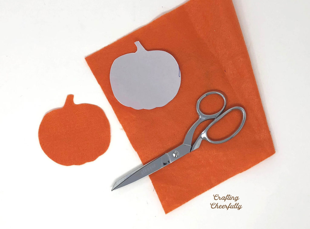 A pumpkin template lays on a sheet of orange felt next to a scissors.
