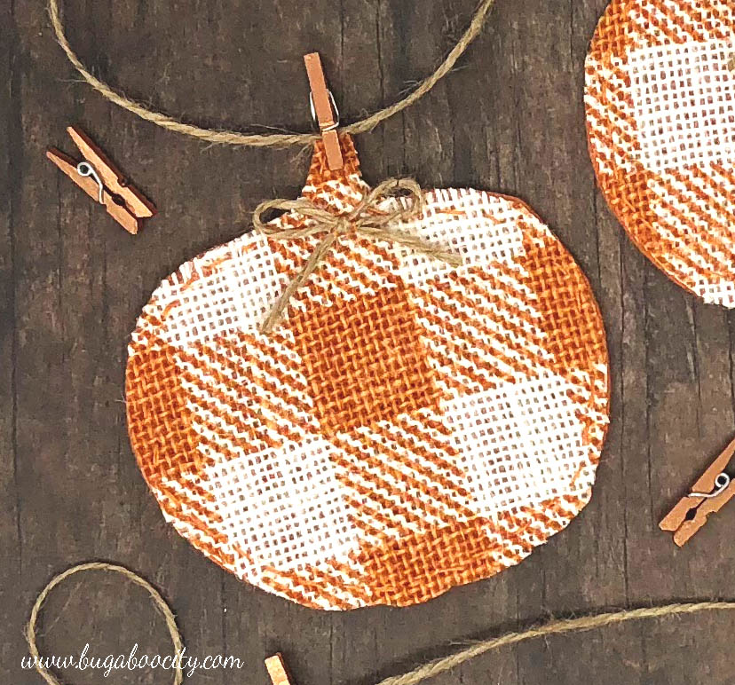 A pumpkin banner pennant made from orange buffalo check burlap is attached to twine with a mini clothespin.