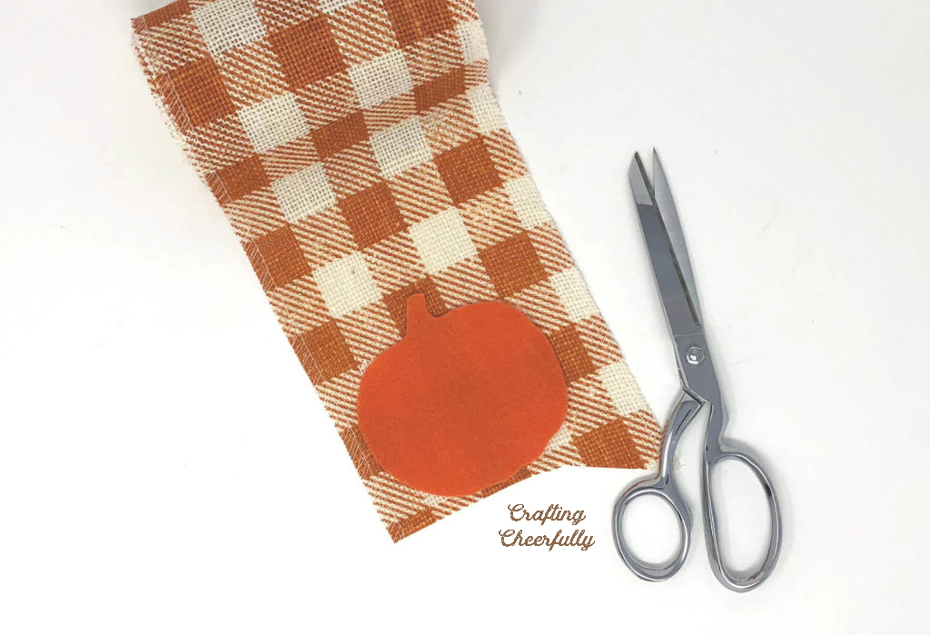An orange felt pumpkin is laid on top of orange buffalo check burlap.