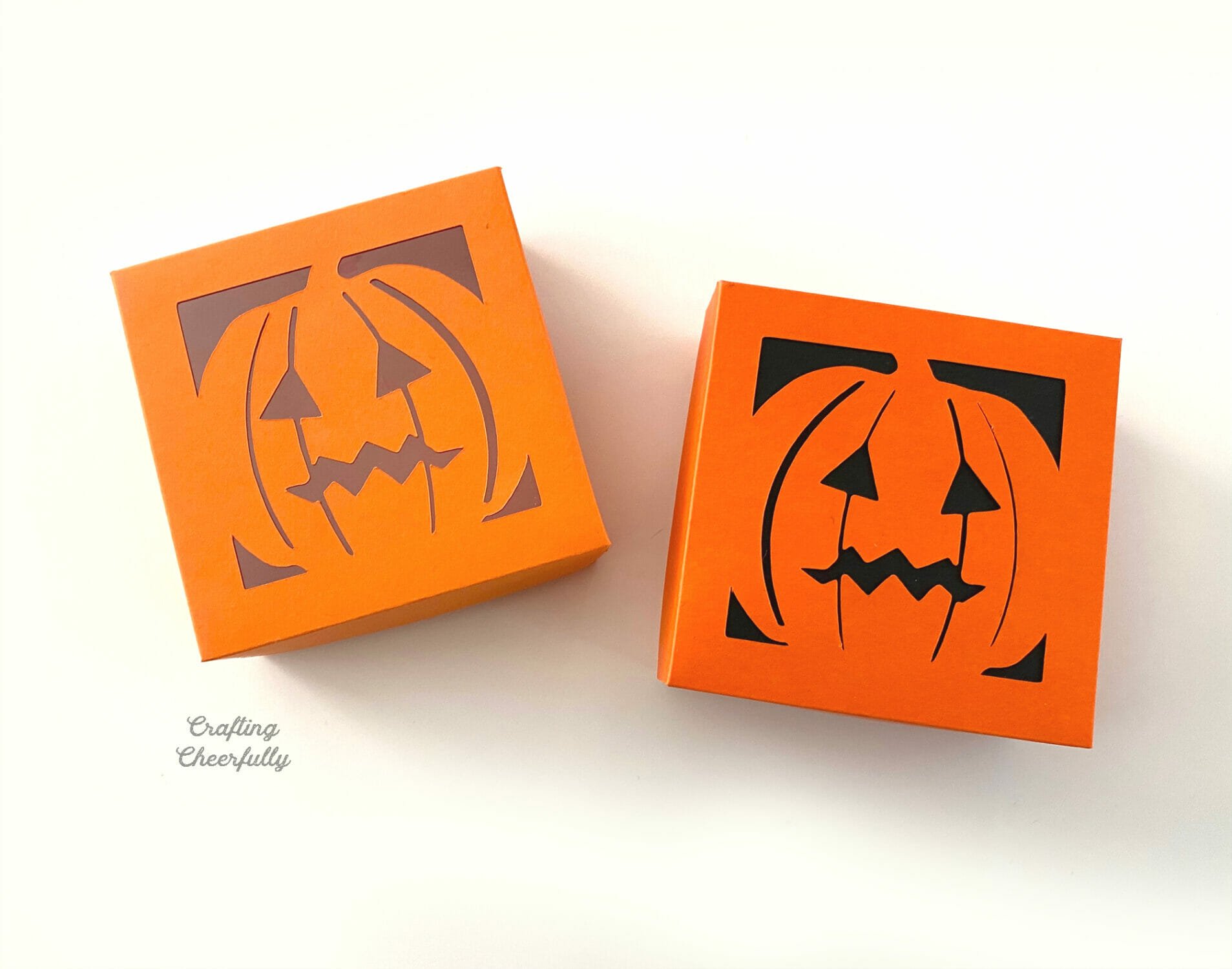 Two pumpkin treat boxes once with a black lid and one with a clear lid sit next to each other.