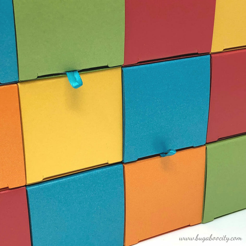 Small square boxes stacked together, two of them have ribbon loops added to the lid openings.