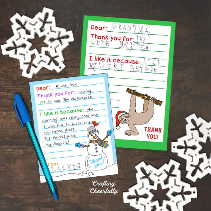 Holiday thank you cards lay on a wooden table with white snowflakes.
