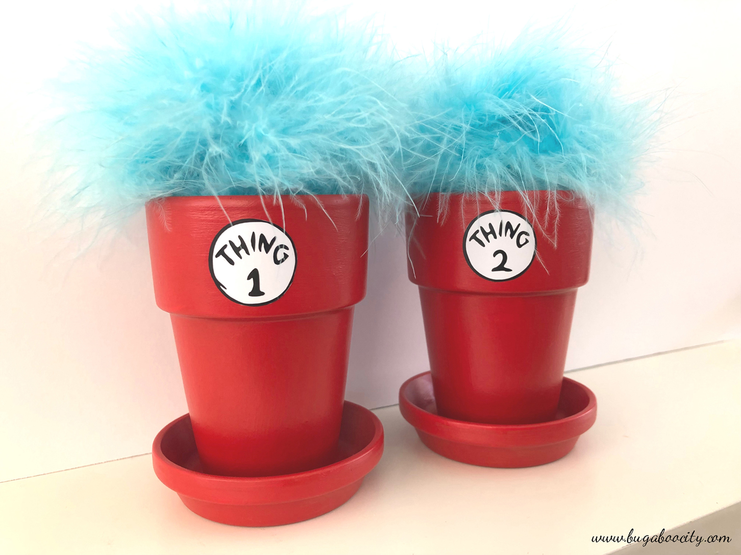 Two red flower pots with blue feathers sticking out of them.