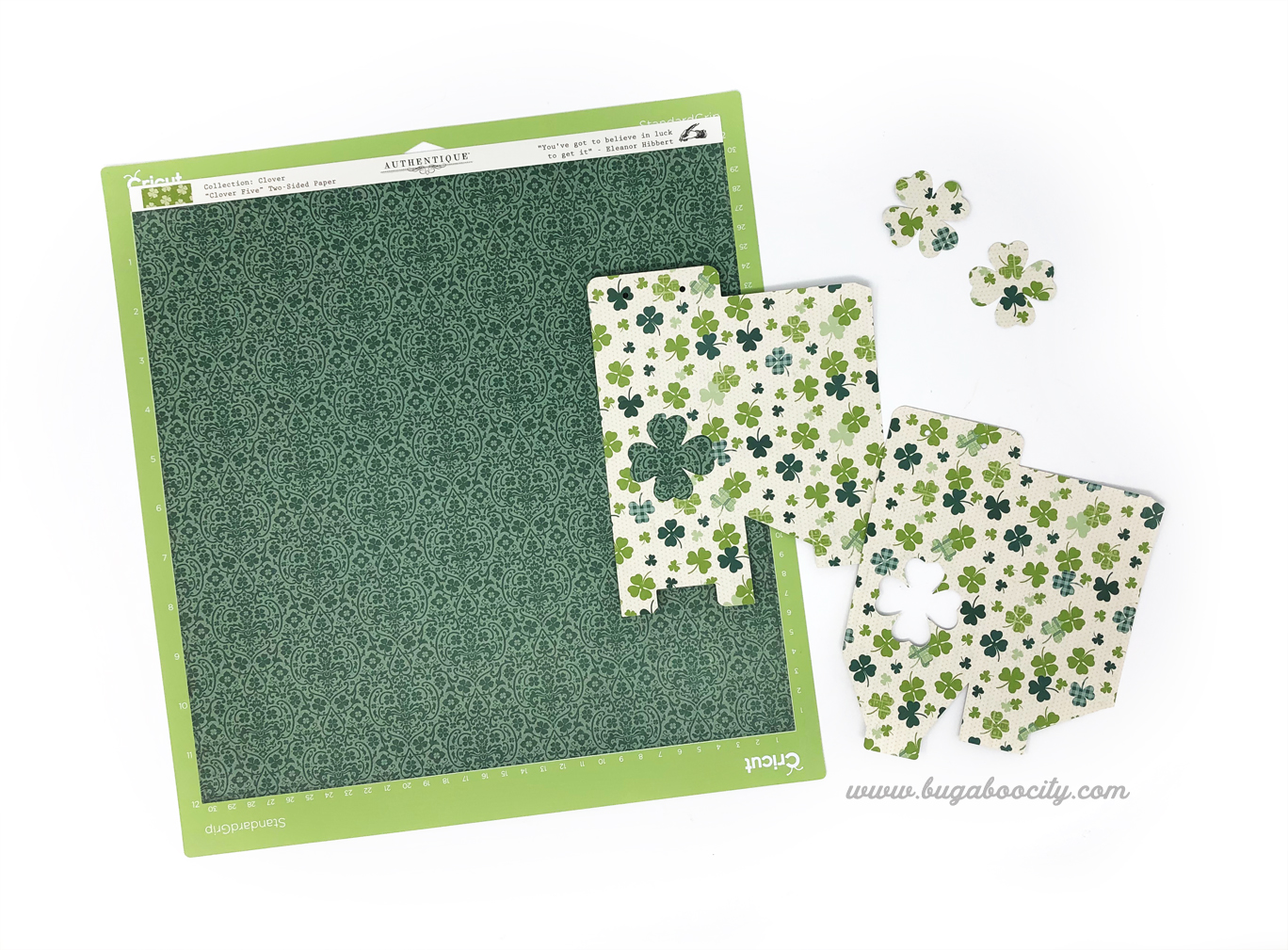 A sheet of green paper on a Cricut cutting mat lays next to a treat box cut from shamrock paper.