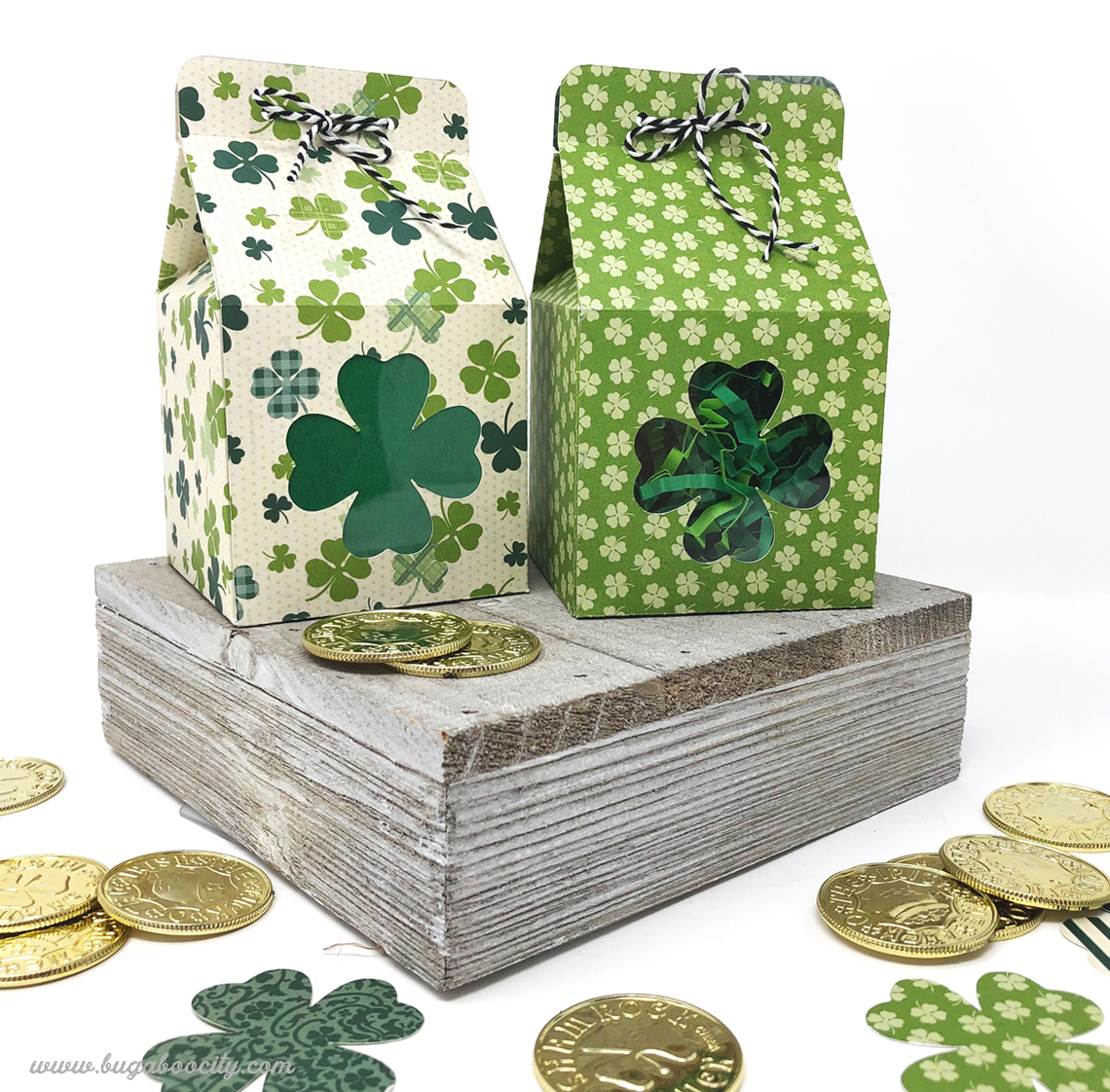 Two St. Patrick's Day treat boxes made from themed paper have shamrock windows in the front.
