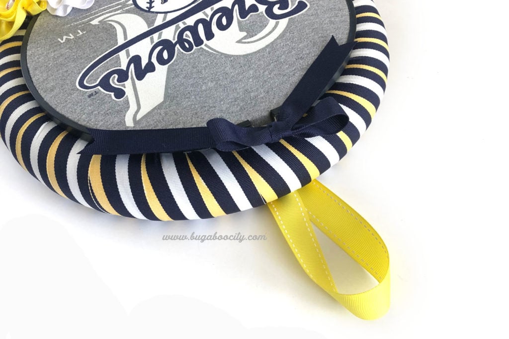 A yellow ribbon loop is attached to the back of the wreath at the top for hanging.