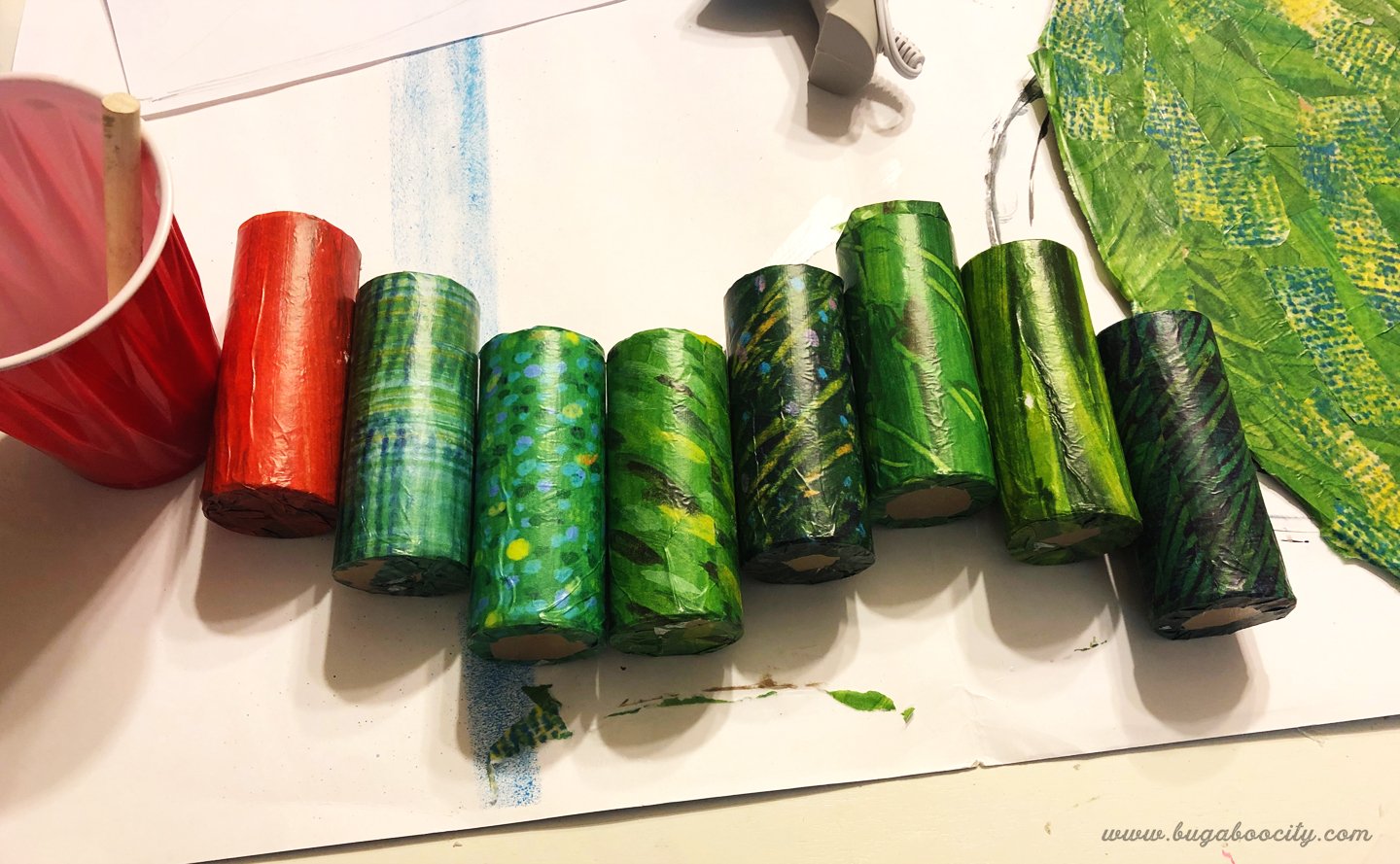 Cardboard tubes covered in green patterned tissue paper; one tube is covered in red tissue paper.