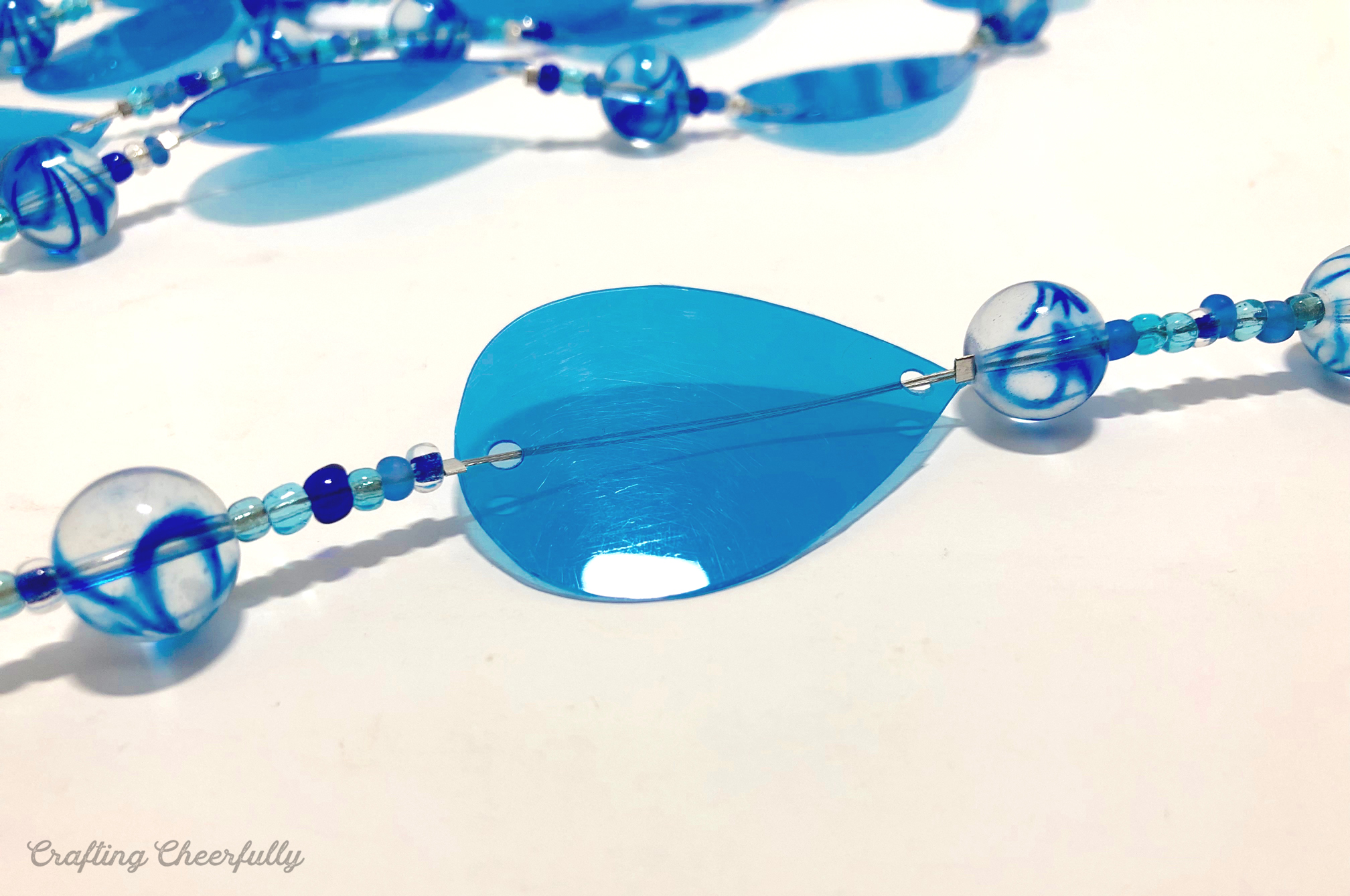 A blue plastic water drop is added to the wire strand with beads above and below it.