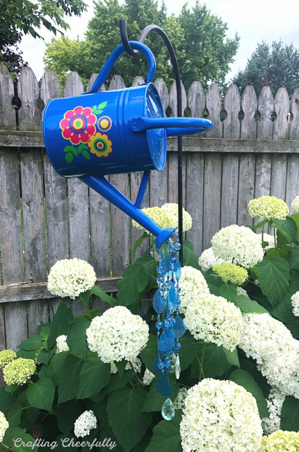 Watering can garden ornament with beads hanging out of the spout.