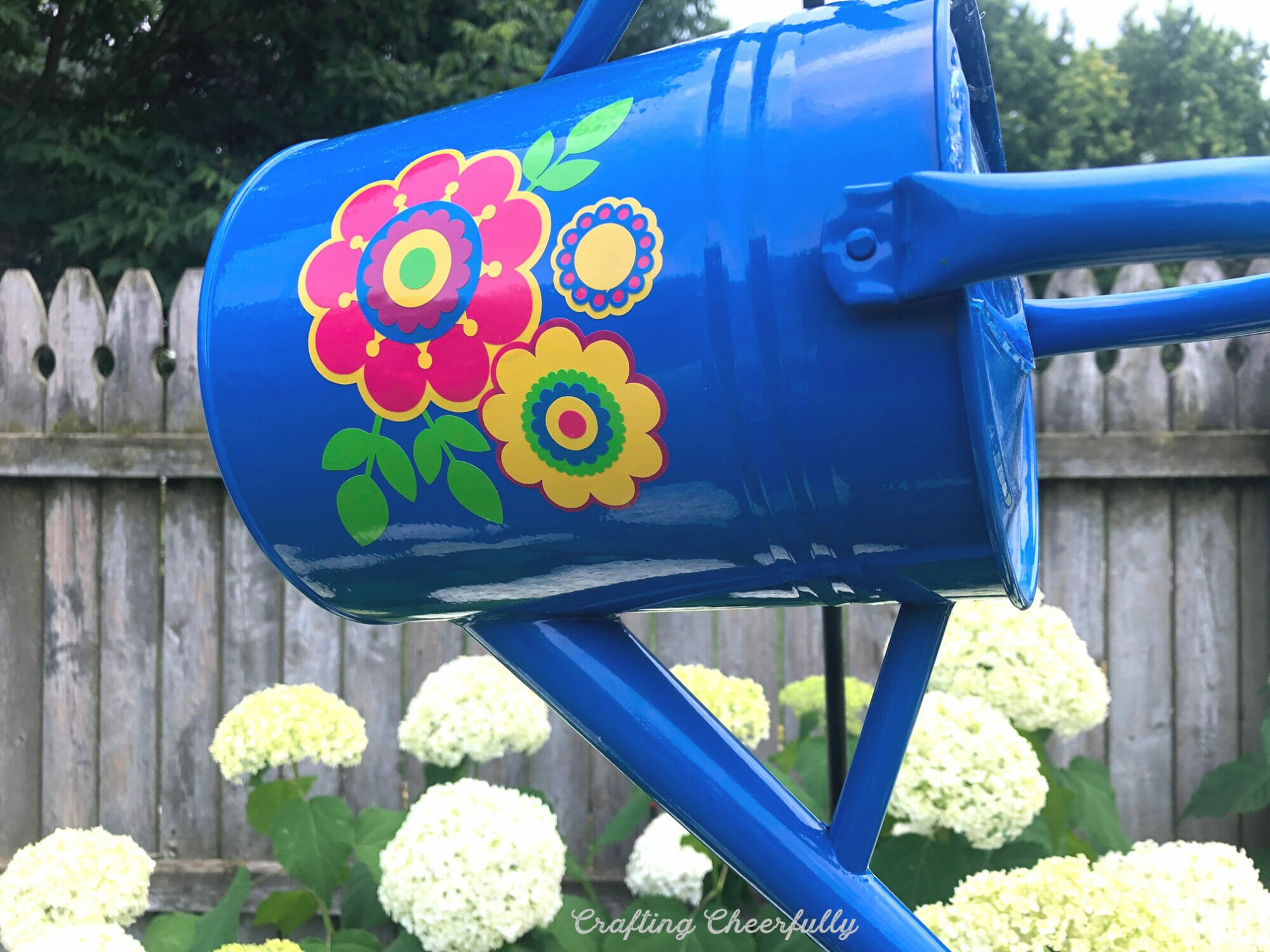 Blue watering can lawn ornament with vinyl flowers on the side.