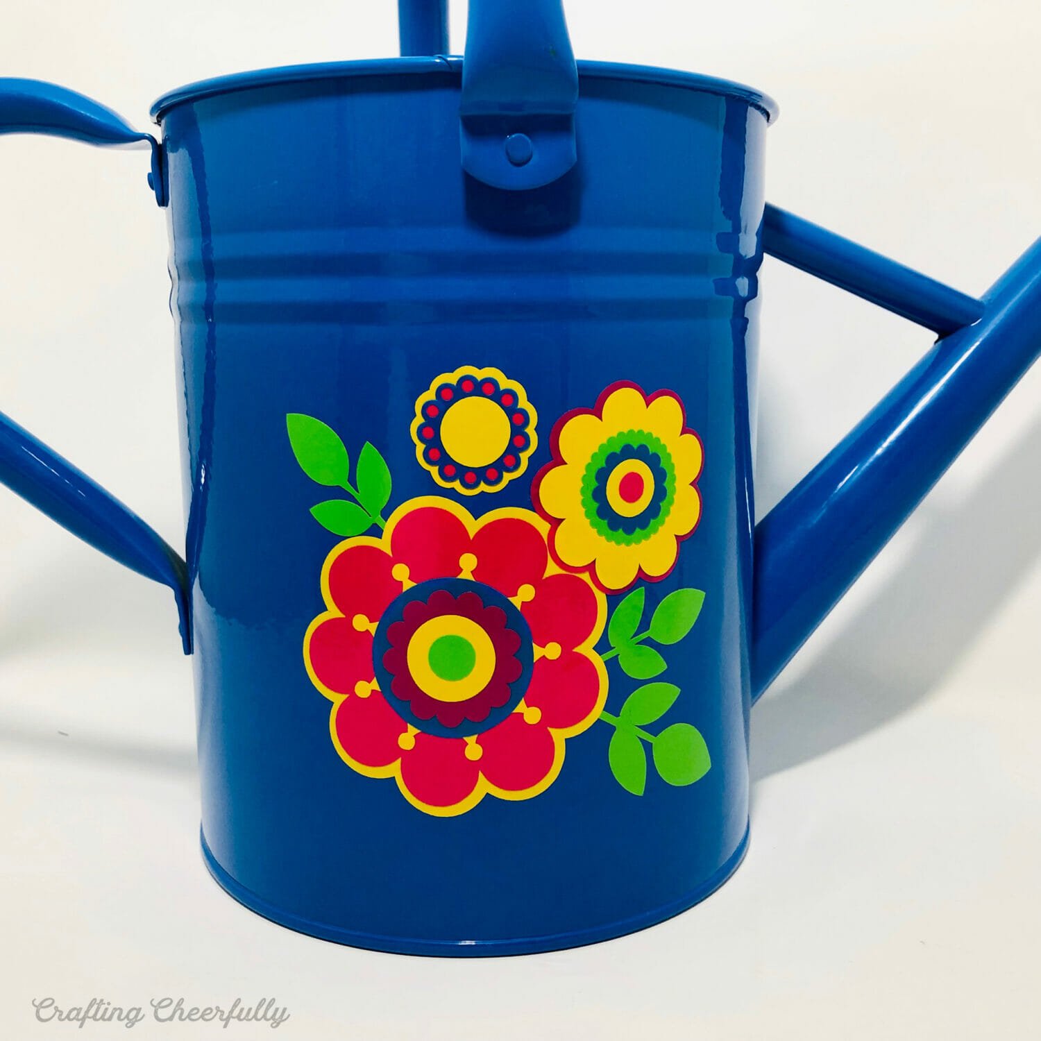 Blue watering can with bright and colorful flower design applied to one side with outdoor vinyl.