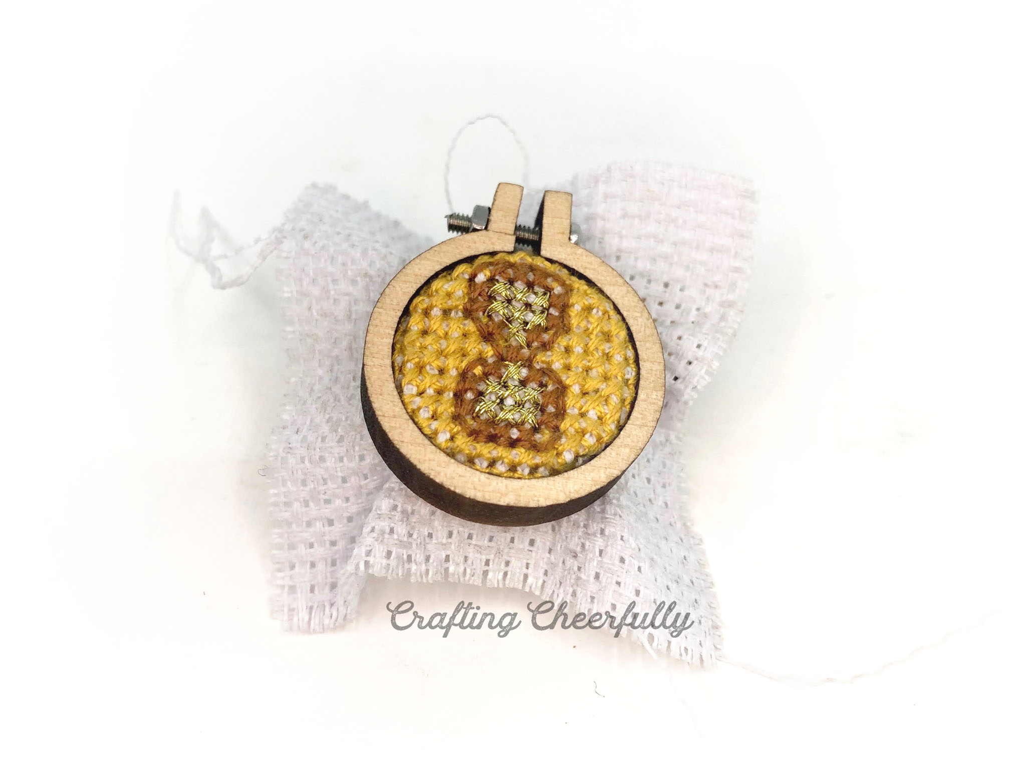 A small cross stitched time turner is stretched in a tiny mini wooden embroidery hoop.