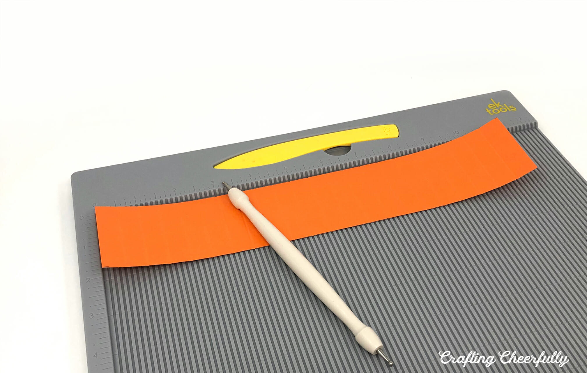 A strip of orange paper is scored on a scoring board.
