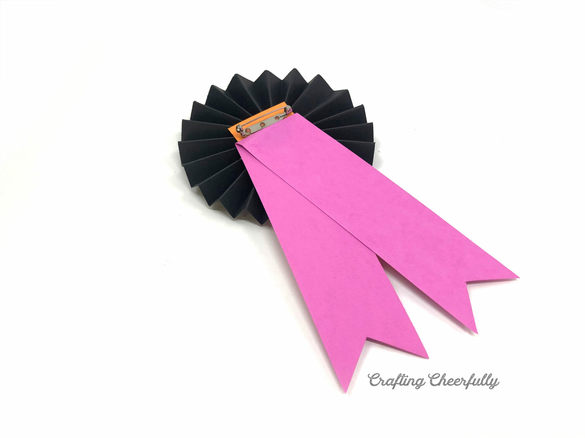 The paper ribbons are attached to the back of a black paper medallion and a pin bar is attached.