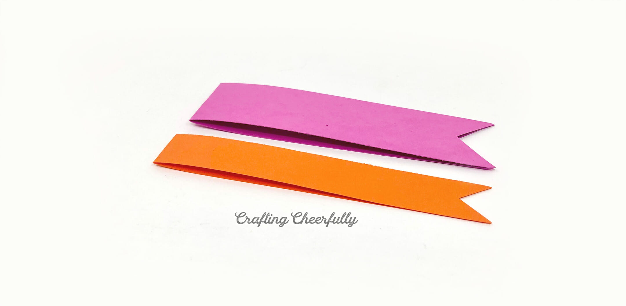 Two strips of paper, orange and purple, are folded in half and have a triangle cut from the bottom edges.