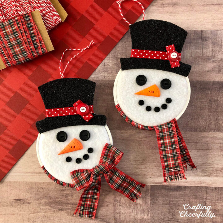 Two snowman hoop ornaments on a wooden table.