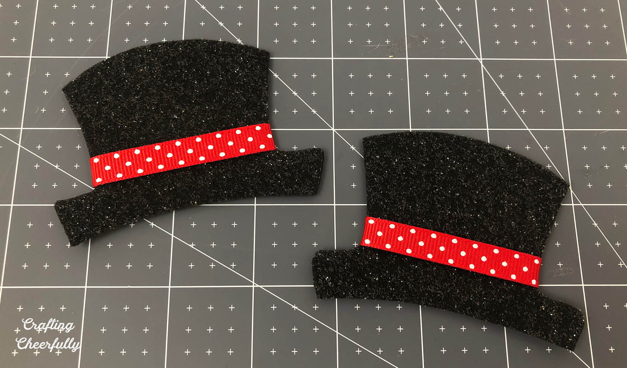 Two hats cut from black glitter felt have a red polka dot ribbon across them.