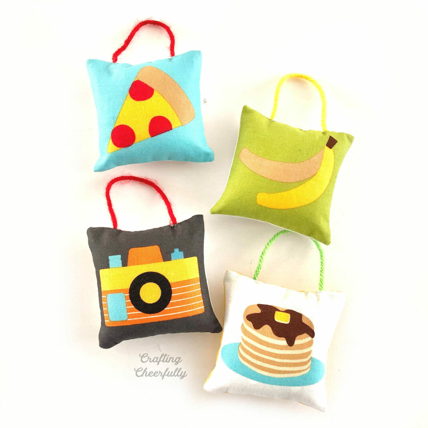 Four fun pillow ornaments featuring cute illustrations on them like a camera, banana, pizza and pancakes!