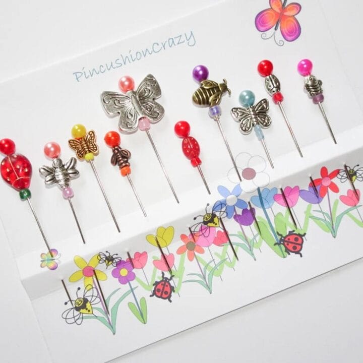 Decorative pins with butterfly and flower charms on the top are in a white piece of cardboard.