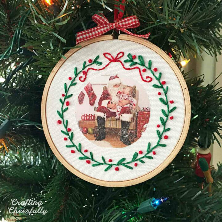 Christmas embroidery hoop ornament hanging in a Christmas tree.