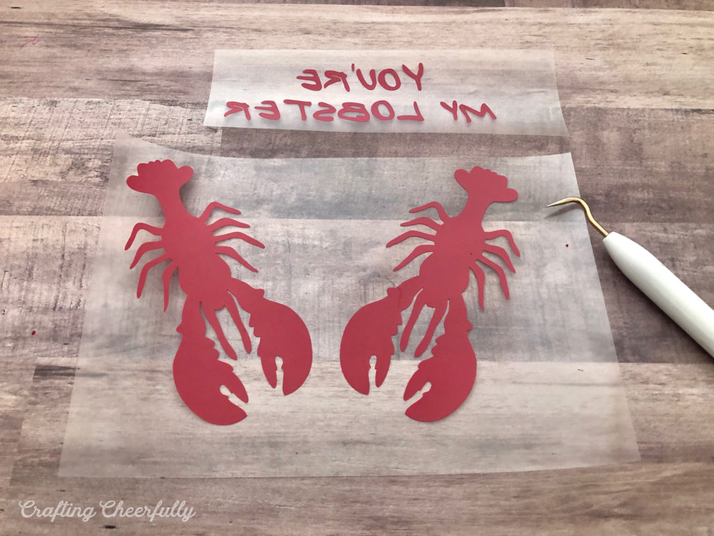 The lobster and text cut from red HTV are weeded with a weeding tool.