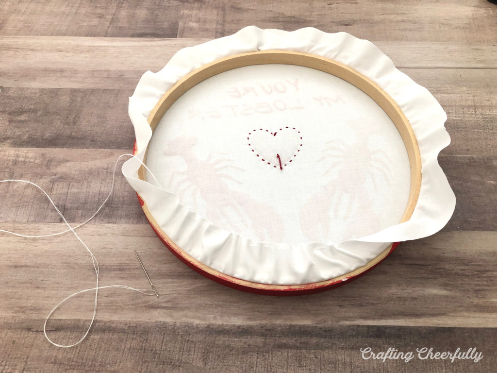 White thread gathers the edge of the white cotton and pulls it in to the back side of the embroidery hoop.