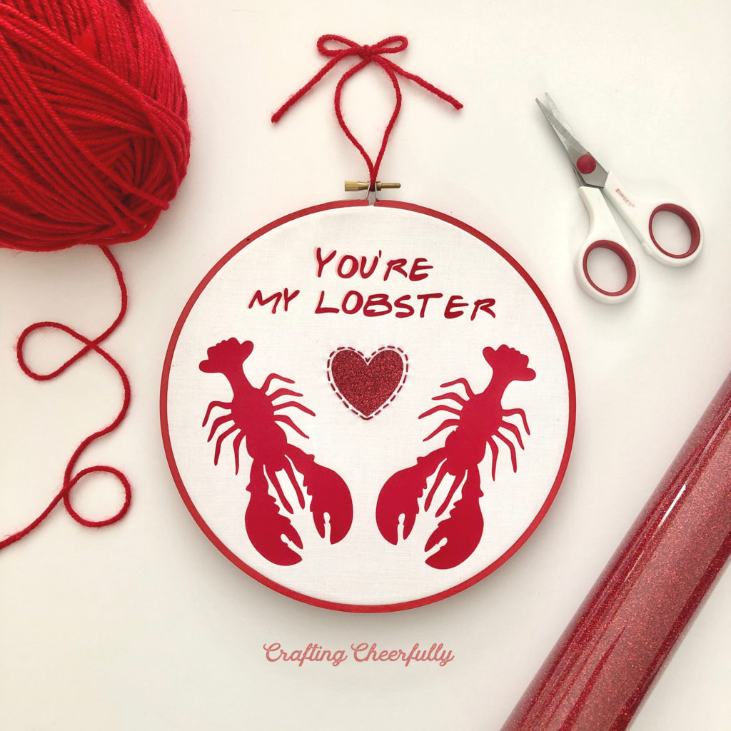 Embroidery hoop with two red lobsters and a glitter heart between them with the words You're My Lobster at the top; everything is made from red Iron-On with hand embroidery around the heart.
