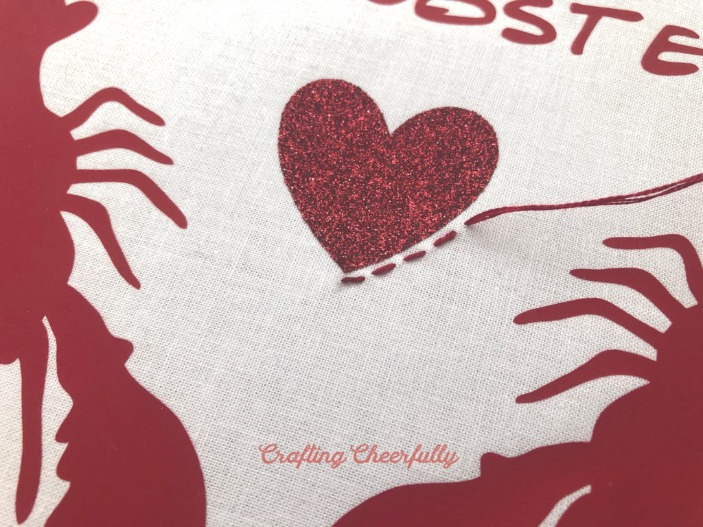 Red embroidery thread is used to create a small running stitch around the glitter heart in the middle of the design.