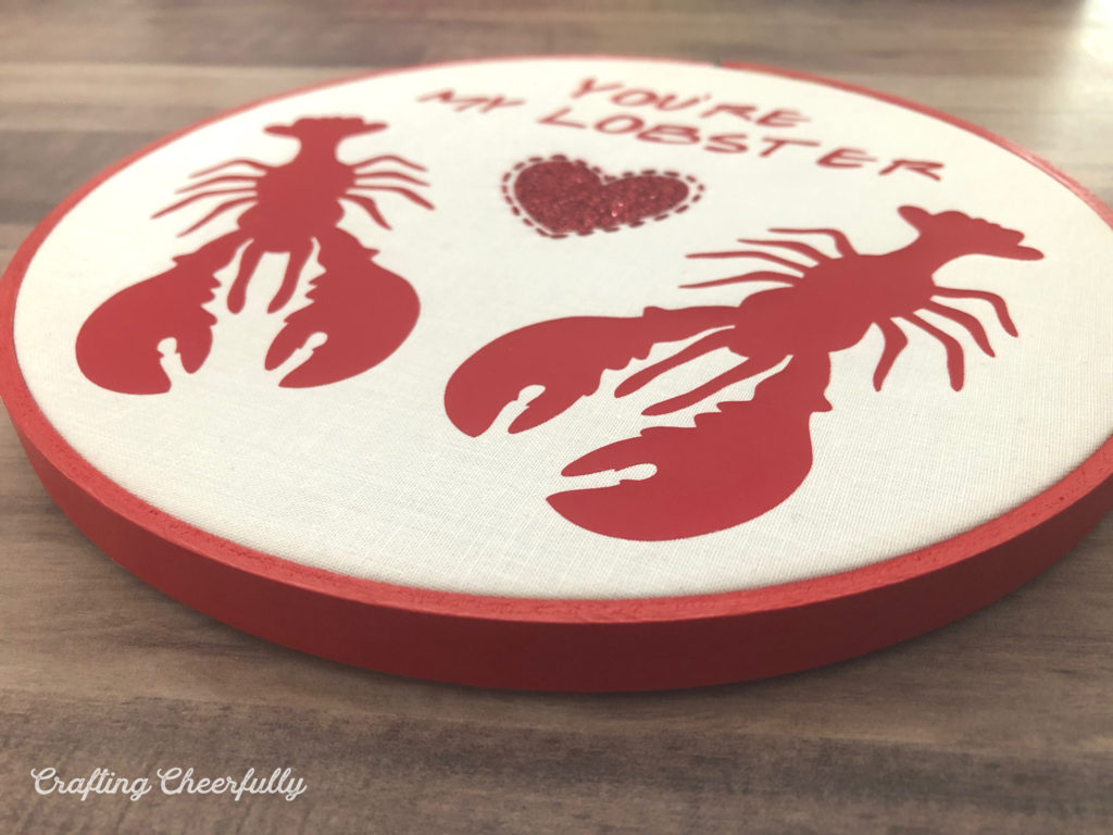 Embroidery hoop with two red lobsters and a glitter heart between them with the words You're My Lobster at the top; everything is made from red Iron-On with hand embroidery around the heart.