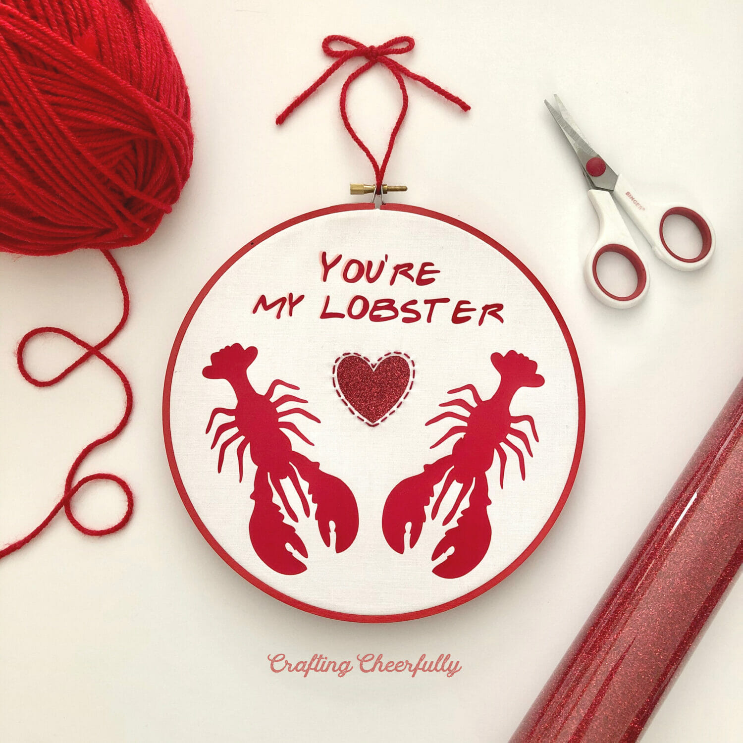 Embroidery hoop with two red lobsters and a glitter heart between them with the words You're My Lobster at the top; everything is made from red Iron-On with hand embroidery around the heart.