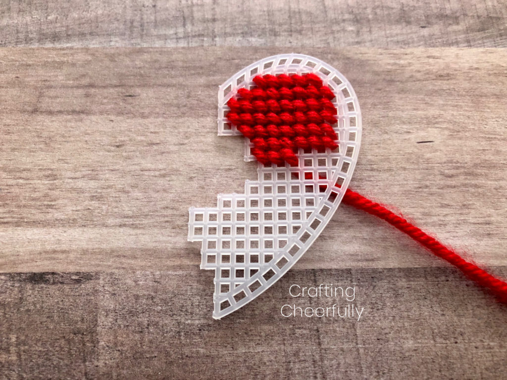 The ride side of the heart canvas with six finished rows of stitching; the seventh is partially complete. All stitches are diagonal from right to left and made with red yarn.
