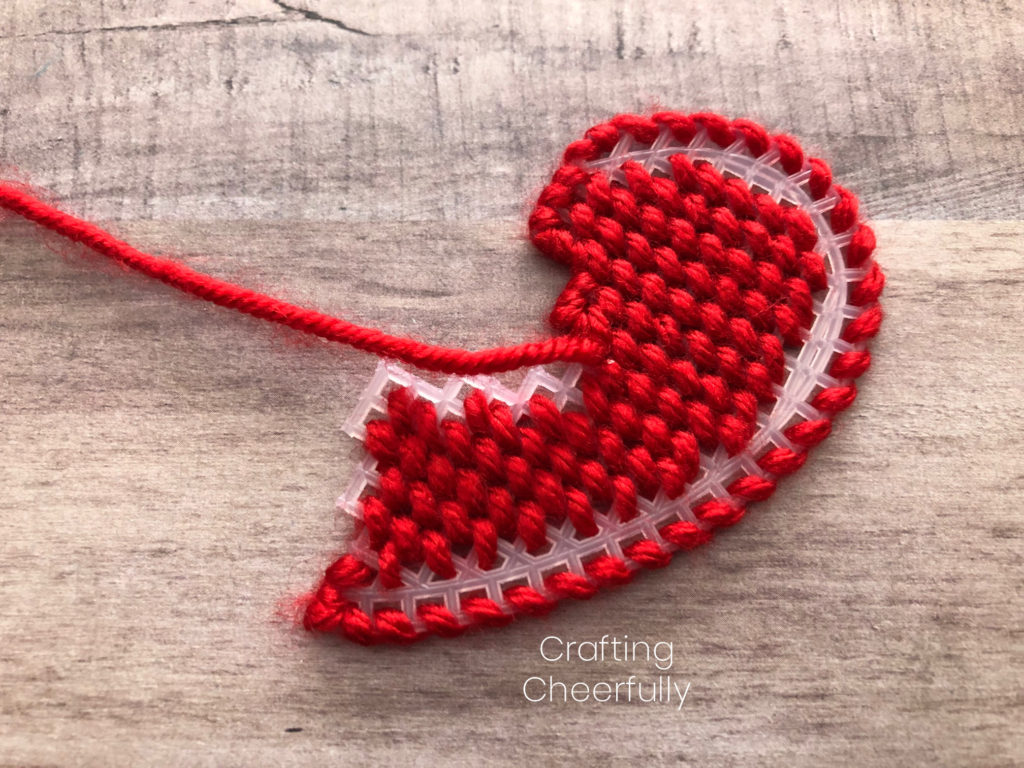 Red yarn is used to stitch around the edges of the plastic heart canvas.