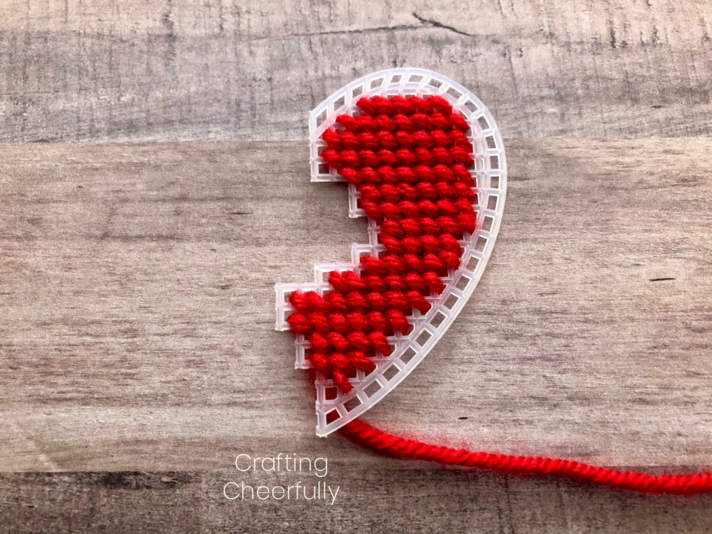 The right side of the plastic heart is stitched with red yarn in small diagonal stitches.