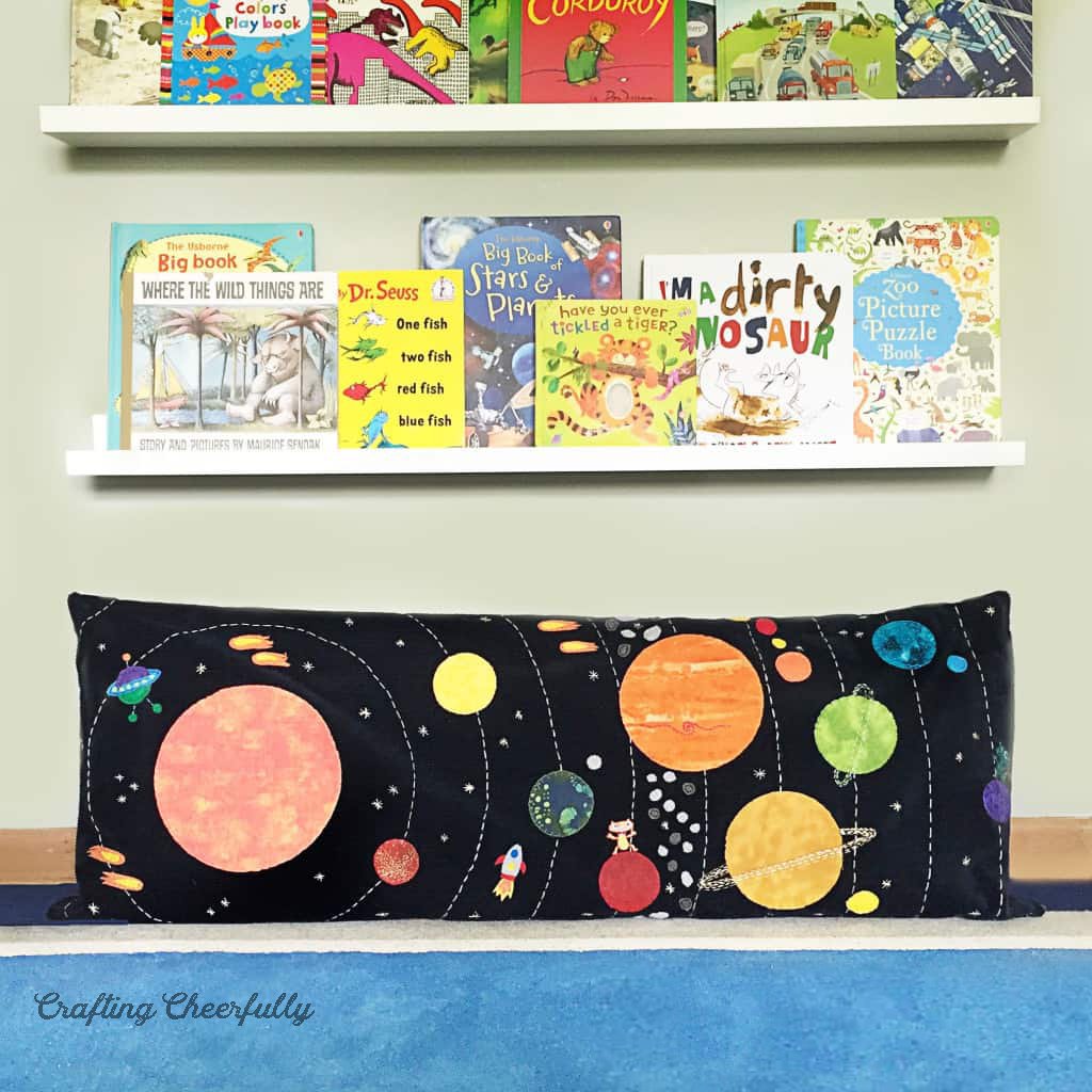 Solar system pillow lays underneath a shelf of books.