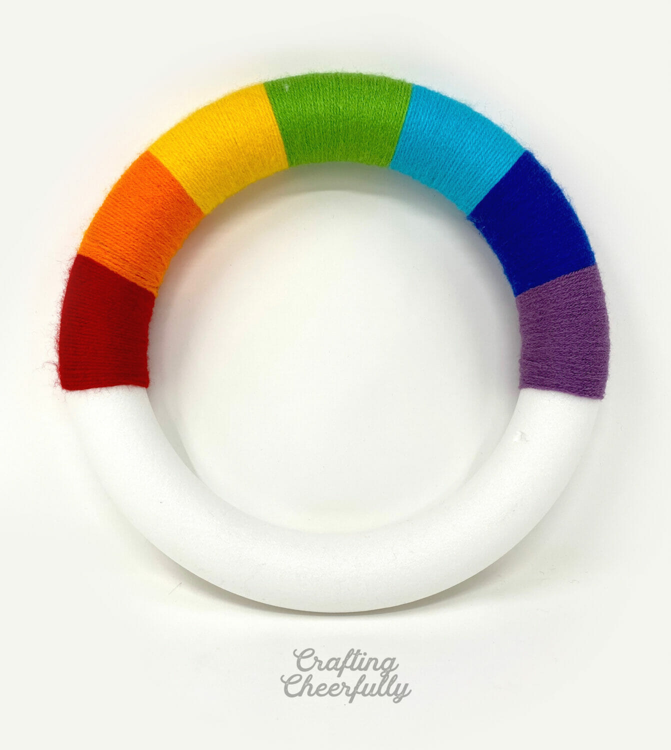 The top of a foam wreath is wrapped in yarn to create a rainbow.