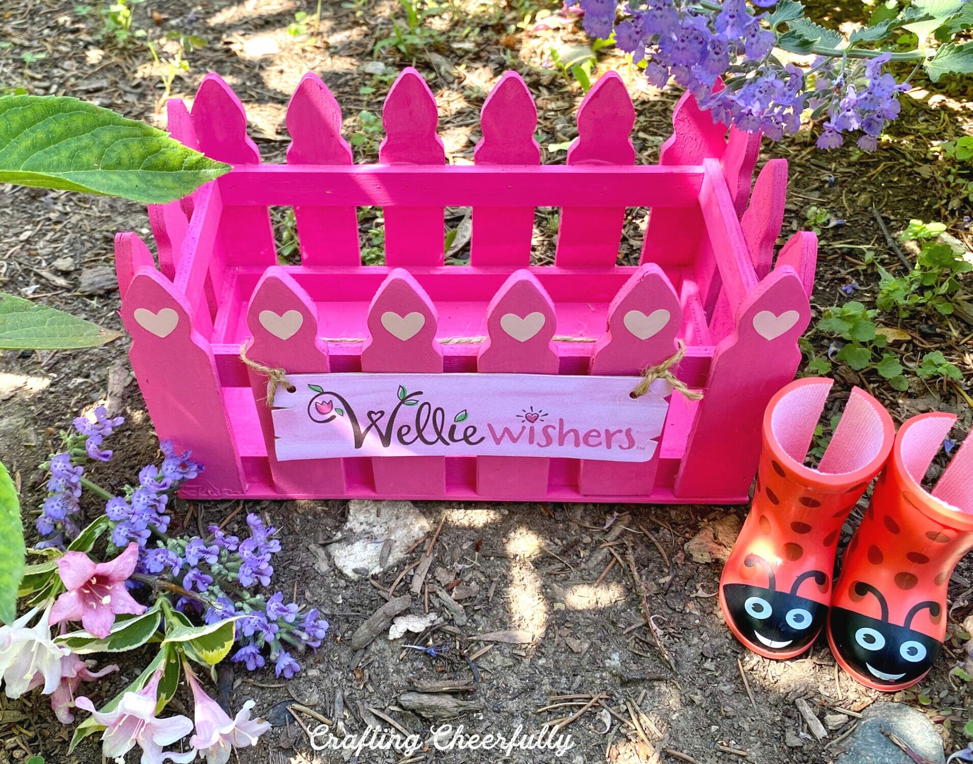 Empty pink picket fence wooden box sits outside in the dirt.