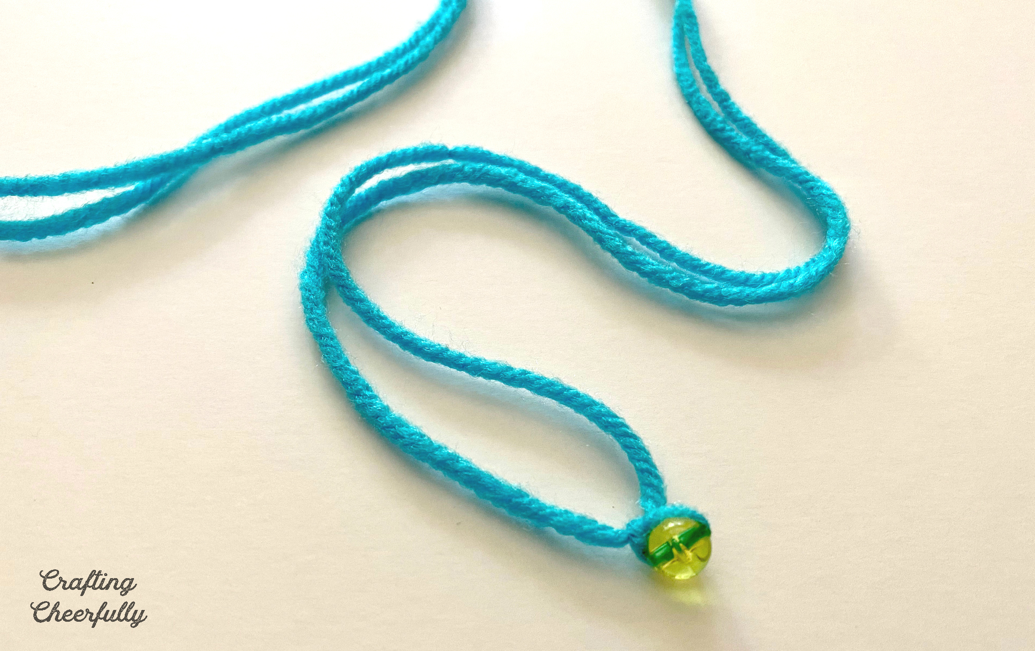 Piece of teal yarn with a bead attached to the middle; the yarn is knotted around it.