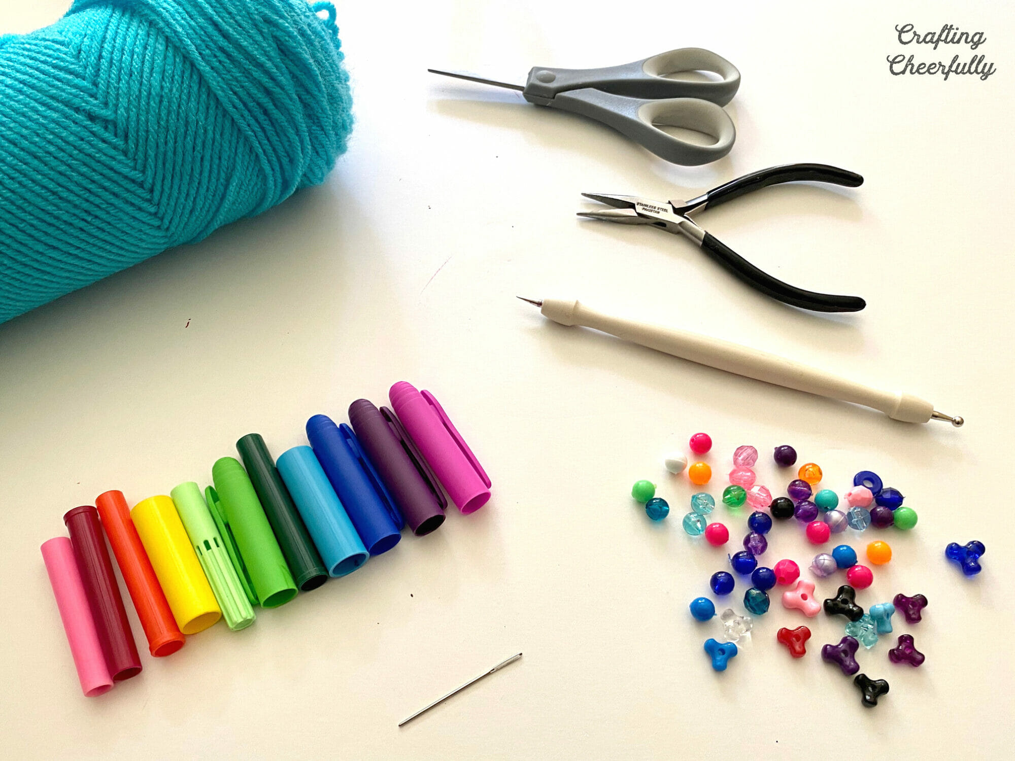 Supplies including yarn, marker caps, beads, scissors, jewelry pliers and needle.