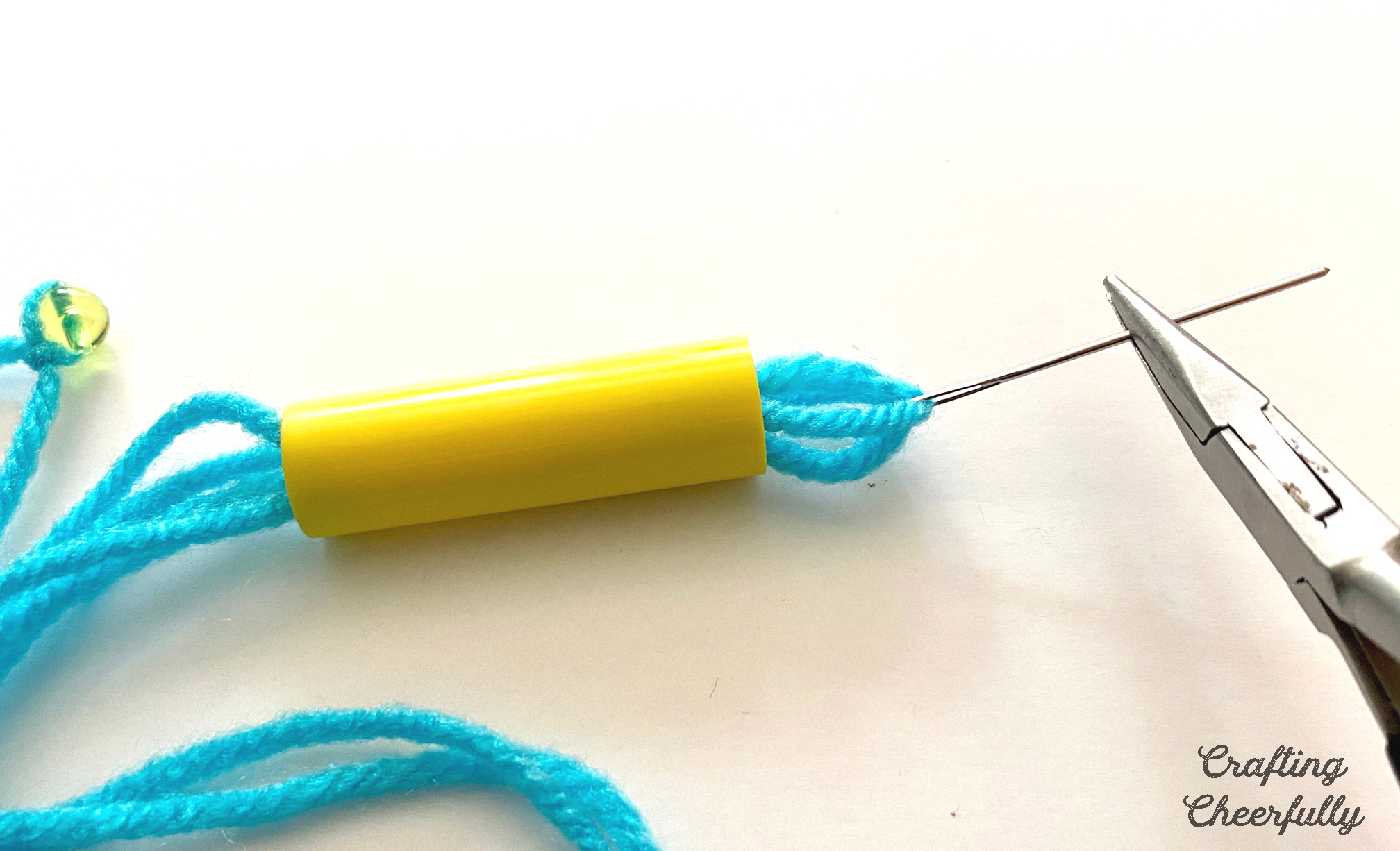 Needle nose pliers is used to pull the needle and yarn through a yellow marker cap.