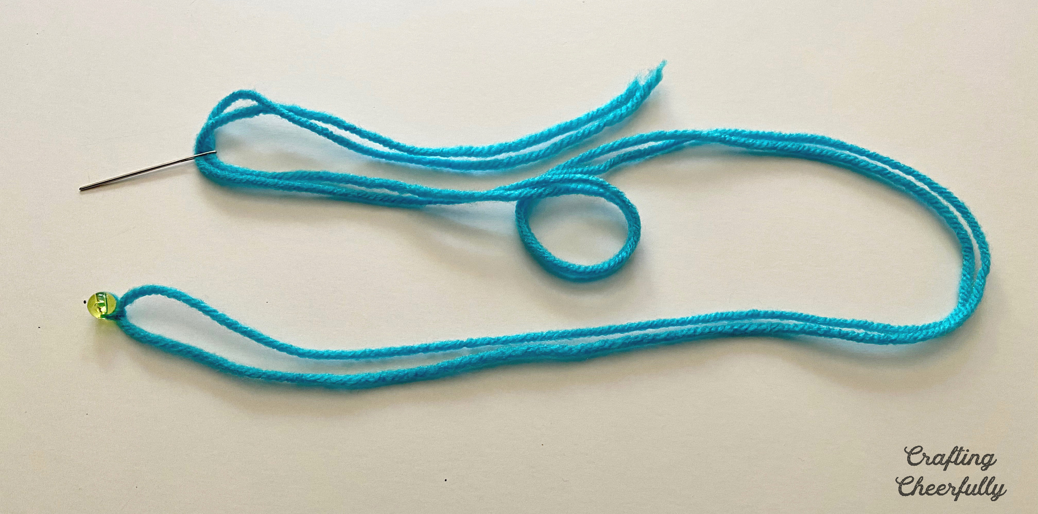 Plastic canvas needle is attached to the end of the teal yarn.