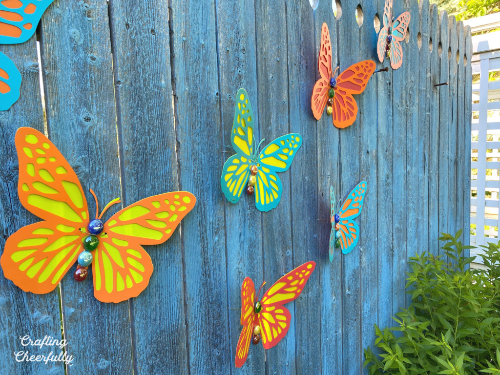 Dimensional and colorful butterflies hang on a blue wooden fence.