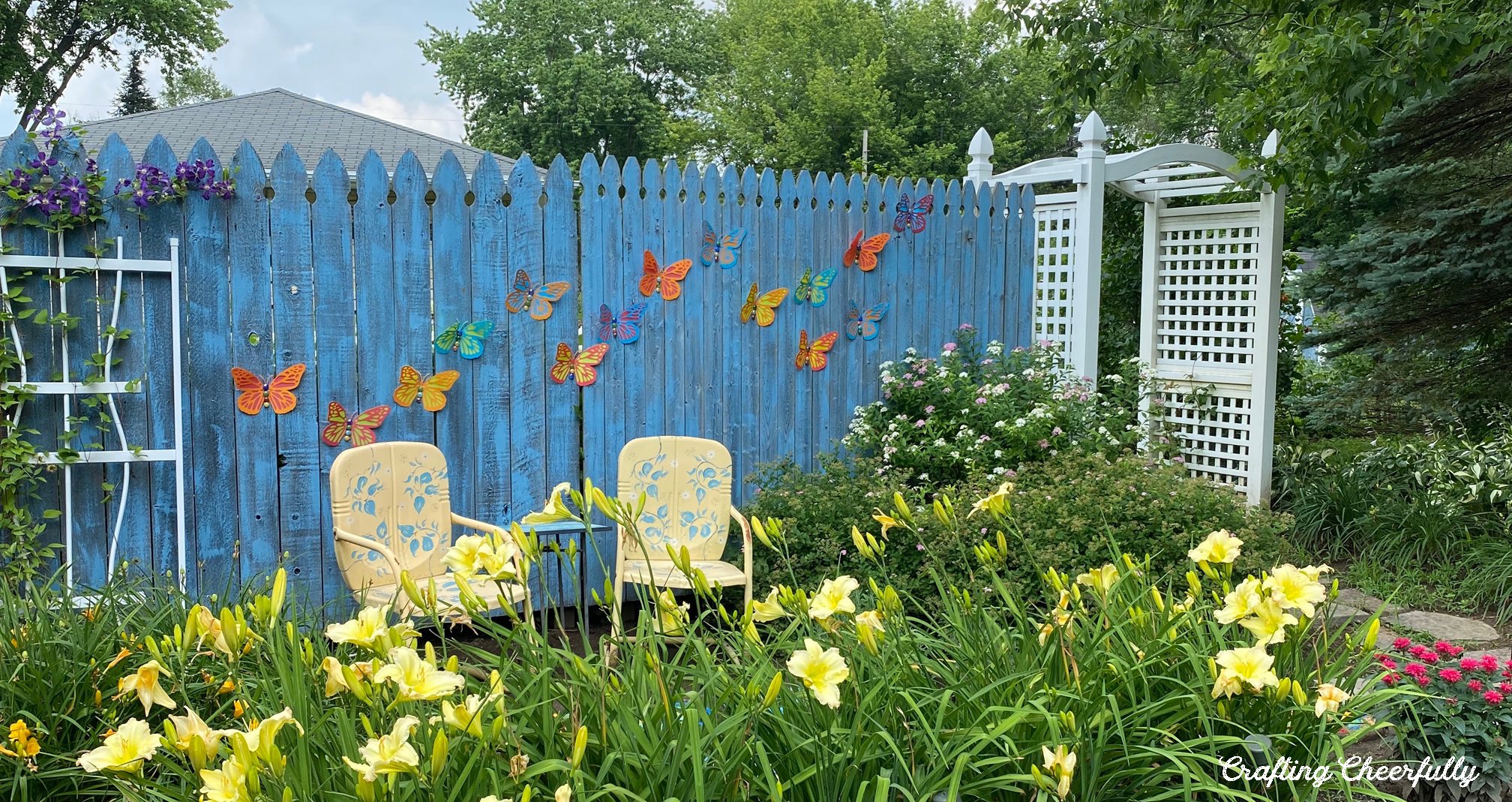 Colorful butterflies hang on a blue painted fence in a garden.