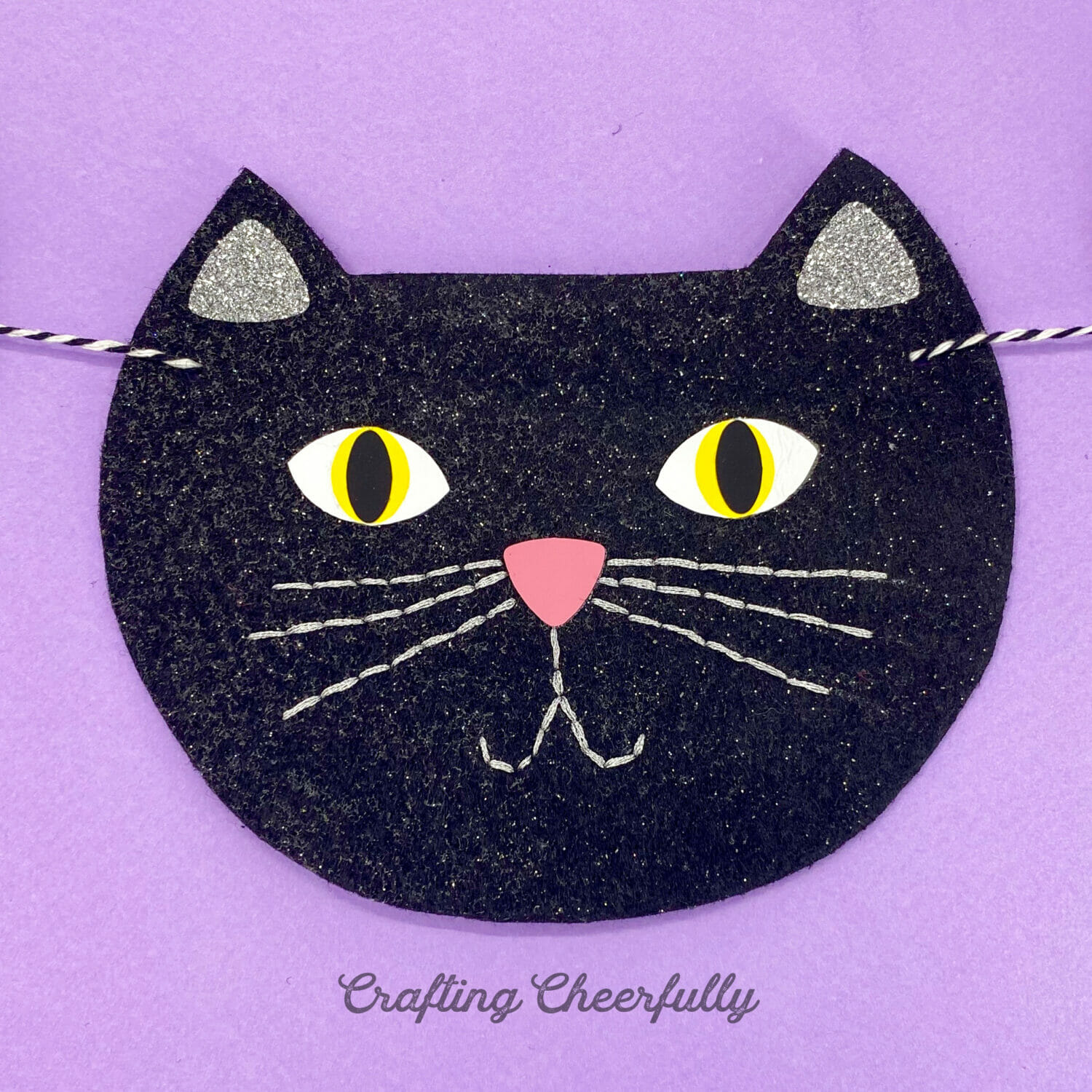 Felt black cat face on a purple background.