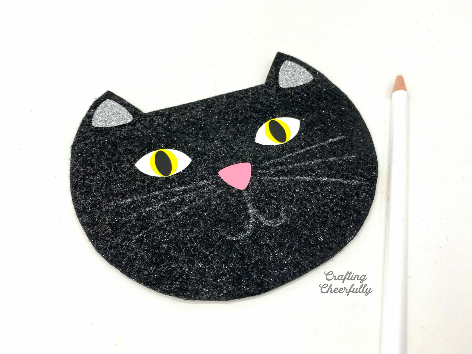 A felt black cat head with the whiskers and mouth drawn in lightly with white pencil.
