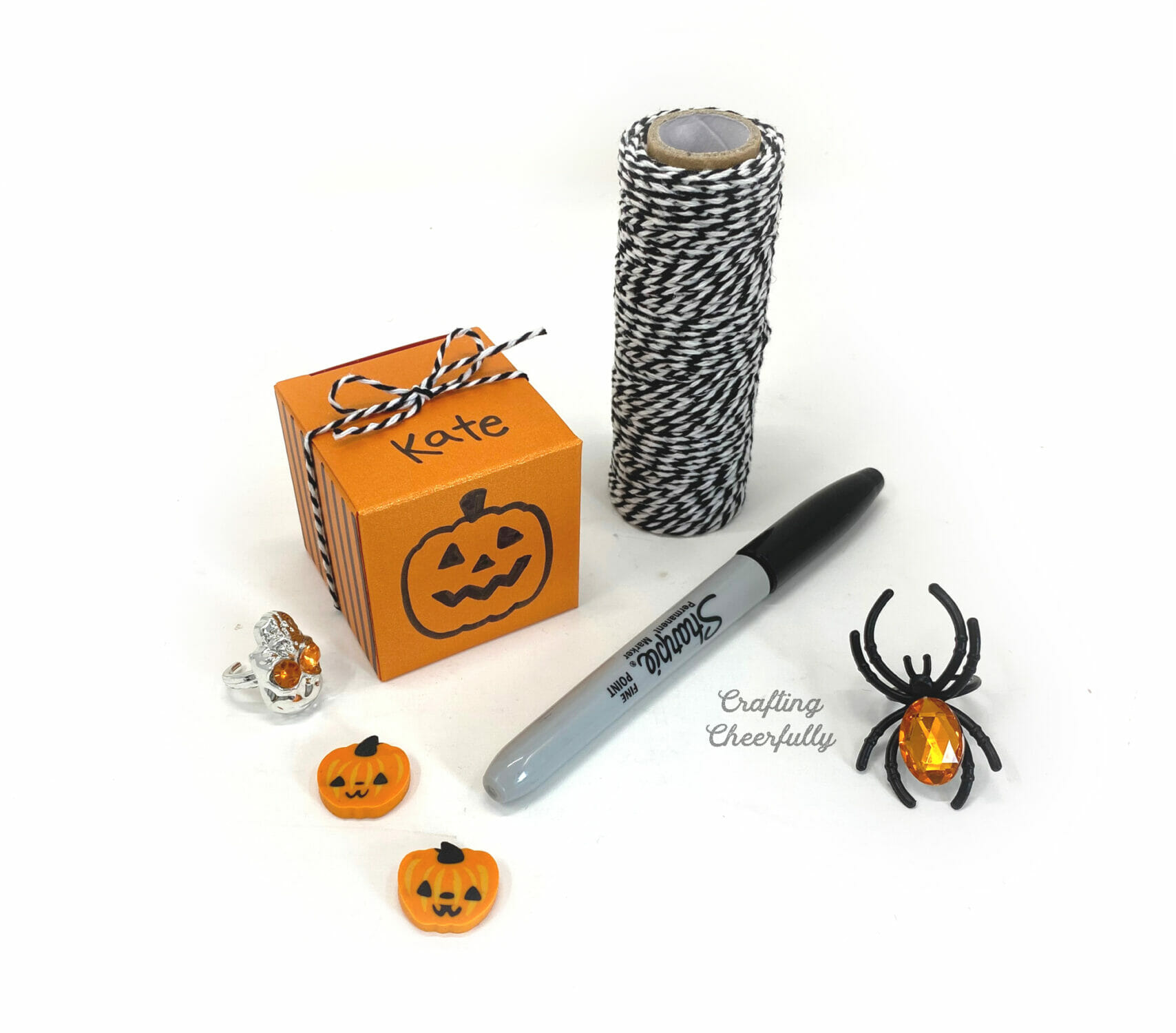 An orange box with a pumpkin dawn on it has the name Kate written across the top of it; it is tied with black and white Baker's twine.