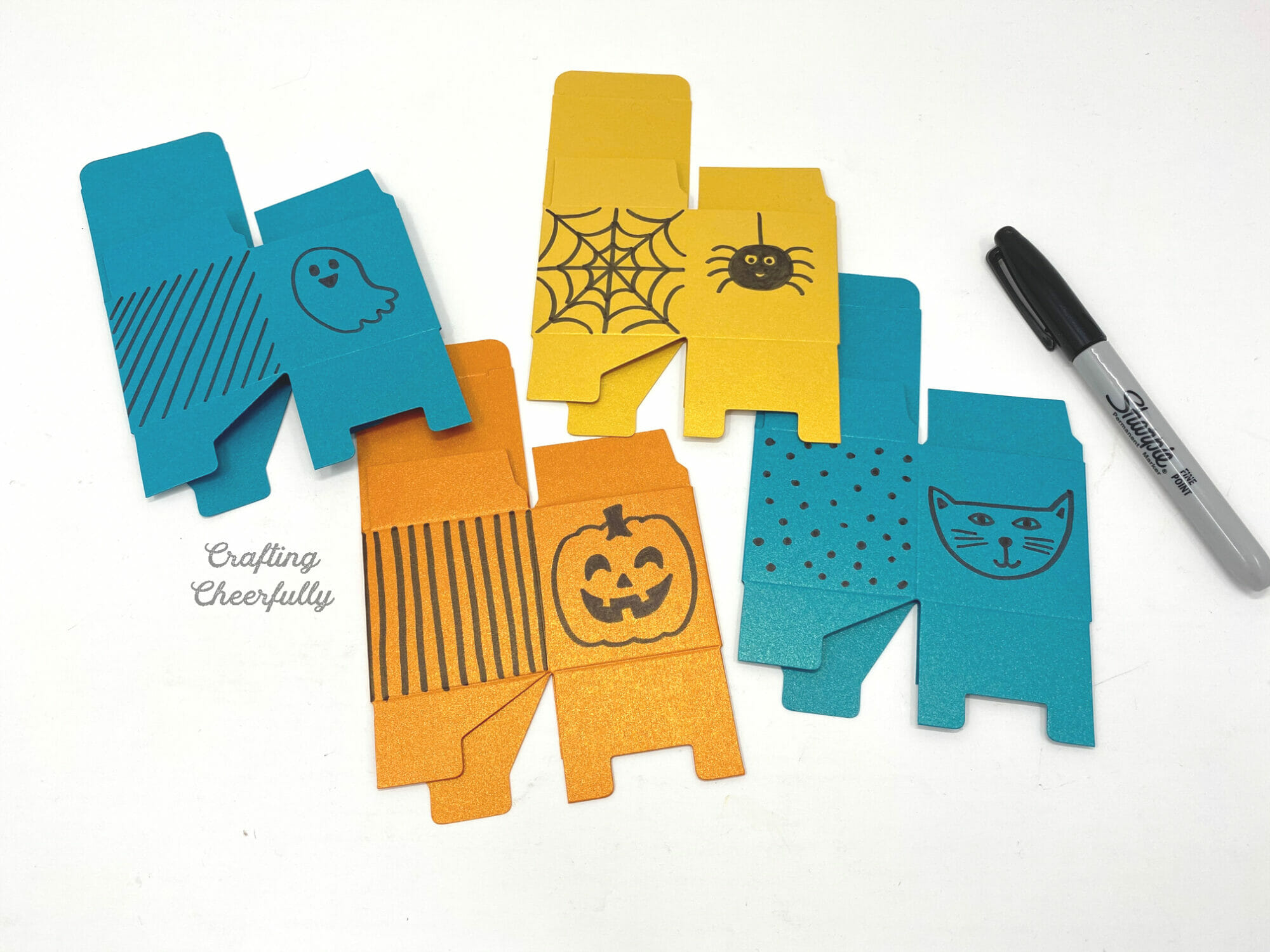 Unopened flat boxes in orange, yellow and teal have Halloween doodles drawn on them including a cat, ghost, pumpkin and spider.